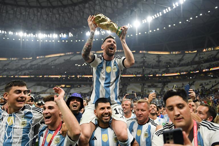 LUSAIL CITY, QATAR - DECEMBER 18: Lionel Messi of Argentina celebrates with the FIFA World Cup Qatar 2022 Winner's Trophy on Sergio 'Kun' Aguero's shoulders after the team's victory during the FIFA World Cup Qatar 2022 Final match between Argentina and France at Lusail Stadium on December 18, 2022 in Lusail City, Qatar. (Photo by David Ramos - FIFA/FIFA via Getty Images)